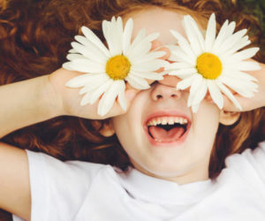 Child with daisy eyes, on green grass in a summer park.